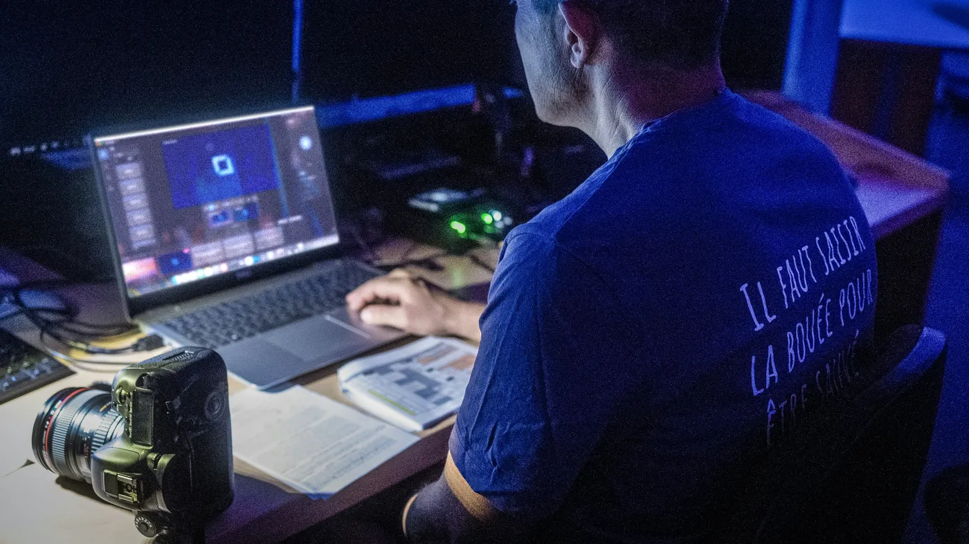 A volunteer in a dark booth runs Verse Copilot on a laptop, with a camera on the desk beside him