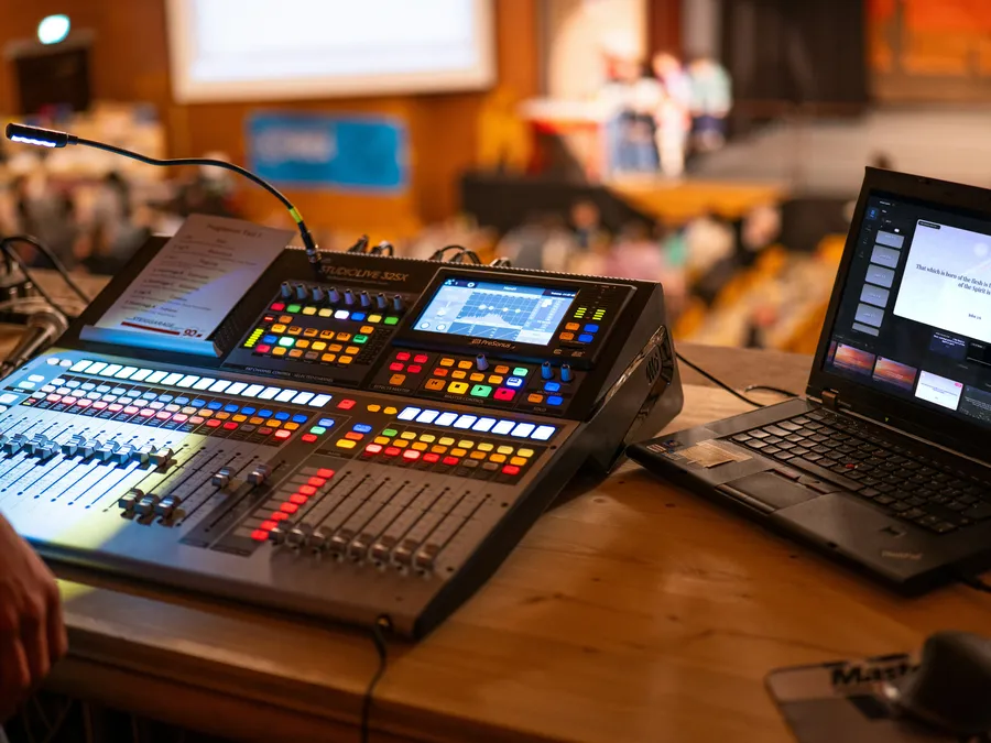 A laptop running Verse Copilot beside the sound board in a traditional sanctuary