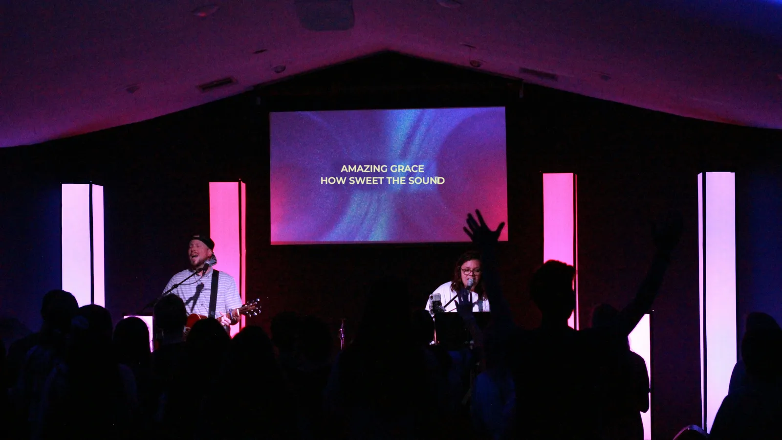 A worship band leading the congregation, with the words Amazing grace, how sweet the sound on the screen above the stage